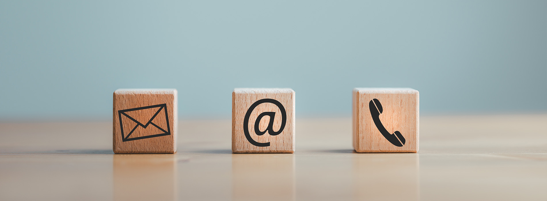 The image shows three wooden blocks with icons representing email, phone, and mailbox, placed on a surface against a blue background.