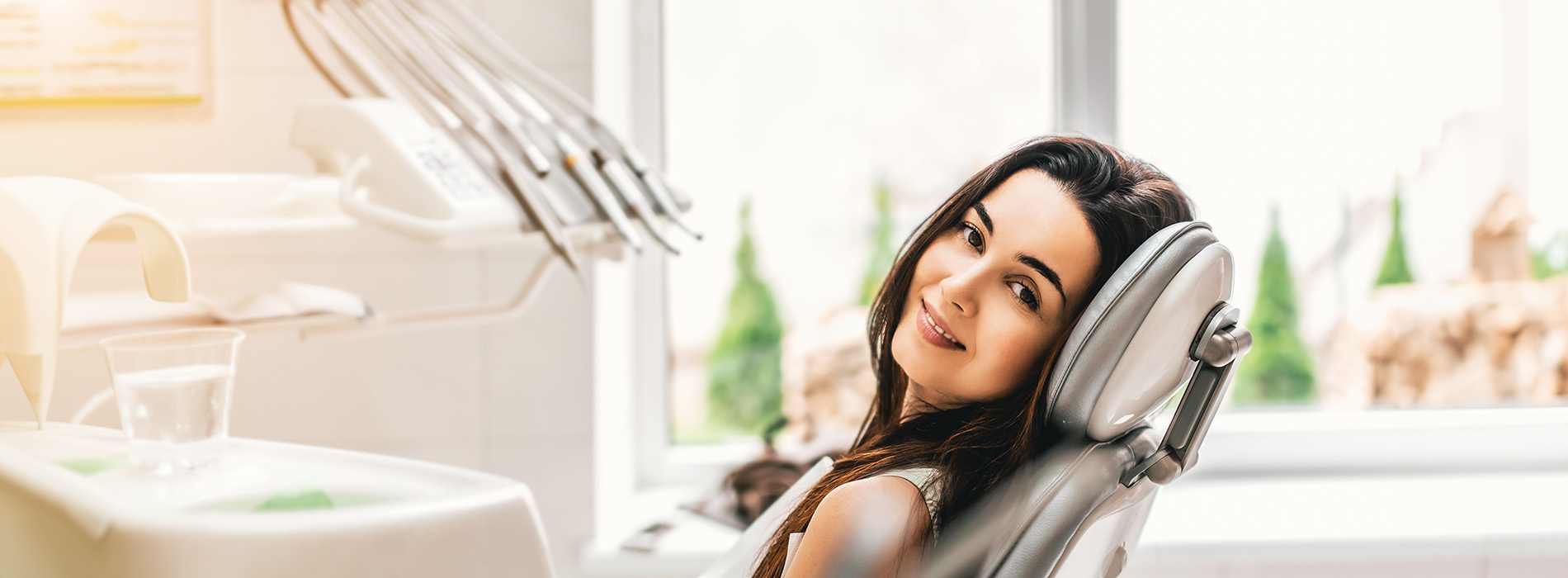 A woman sitting in a dental chair with a smile on her face, looking directly at the camera, surrounded by dental equipment.