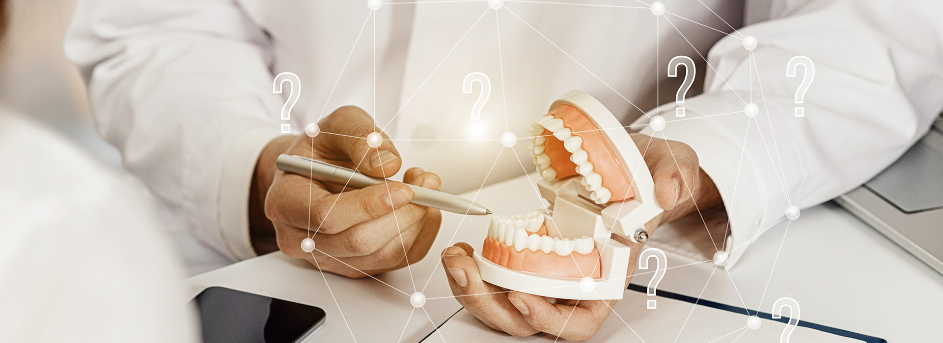 The image shows a dental professional examining a set of teeth on a digital display, with the person s hand holding the model teeth and a pen in their other hand, suggesting a consultation or examination process.