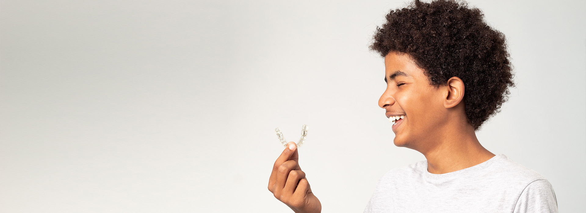 The image features a young person with an afro hairstyle holding a flower in their hand, smiling towards the camera against a plain background.