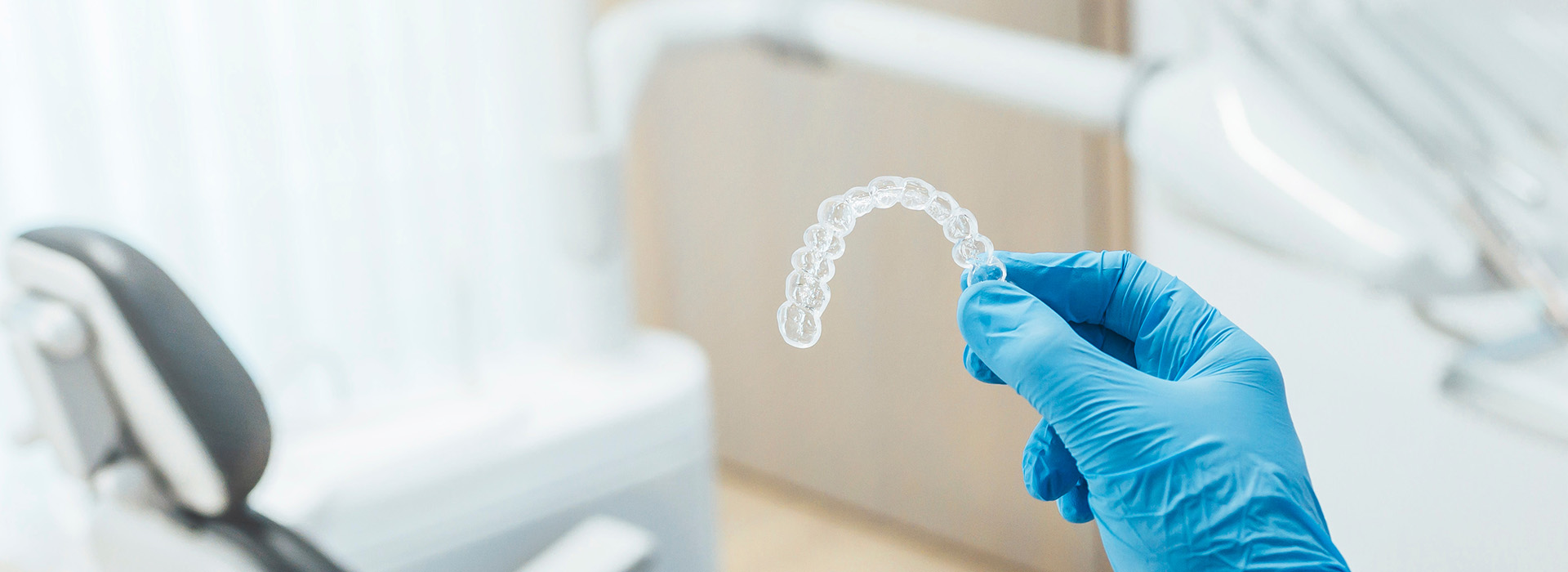 The image shows a transparent plastic model of a mouth being held by someone wearing blue gloves, with dental equipment in the background, suggesting an educational or demonstration context related to dental care or oral hygiene.