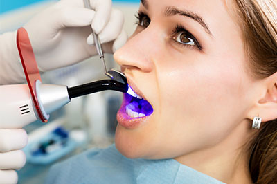 The image shows a person sitting in a dental chair with a device attached to their mouth, likely for a dental procedure, while a dental professional is using a handheld tool on them  they are wearing gloves and a protective face mask.
