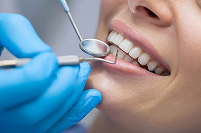 A dental professional performing oral care on a patient s teeth while wearing protective gloves and using dental tools.