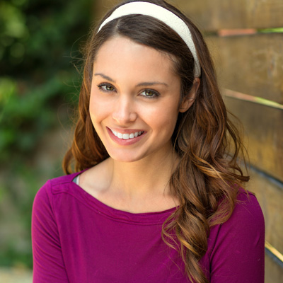 A woman with long hair wearing a purple top and a headband smiles at the camera.