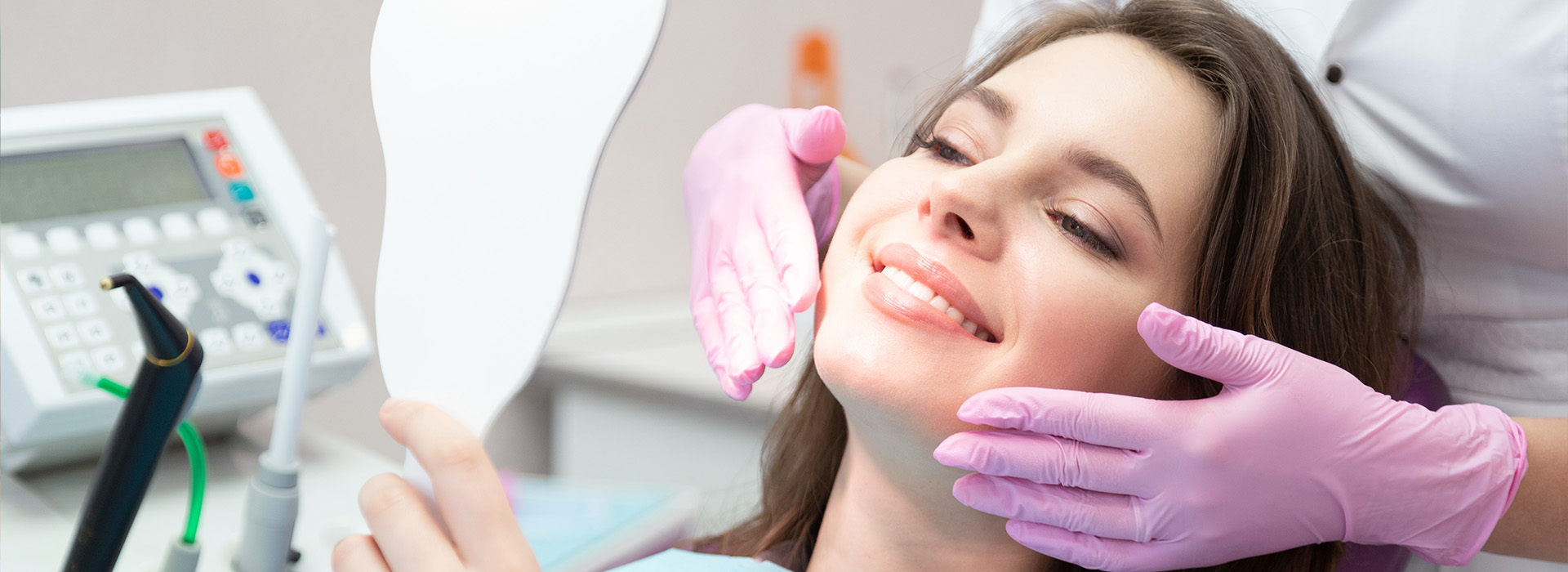 A woman sitting in a dental chair with a dentist s hand adjusting her mouth, both wearing surgical gloves and masks.