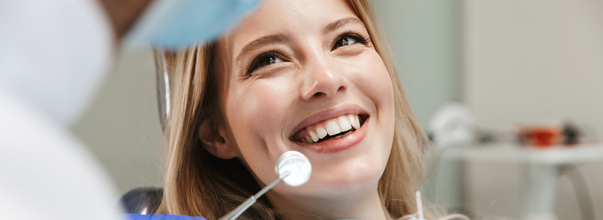 A woman with a bright smile sitting in front of a dental professional during a dental appointment.