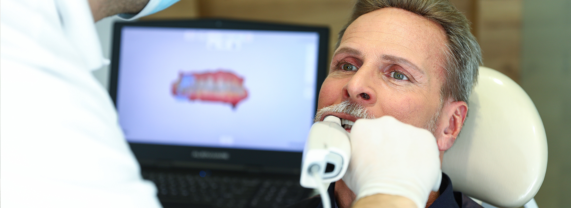 A man receiving dental treatment with a dental professional using a computer screen.