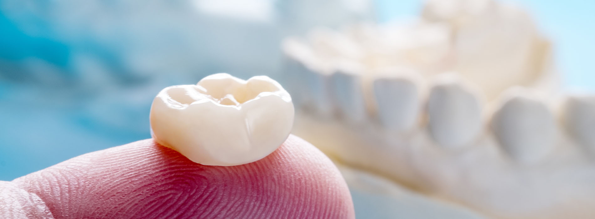 An alt text description of an image featuring a white tooth held up by a hand against a blue background with a watermark visible on the bottom right corner.