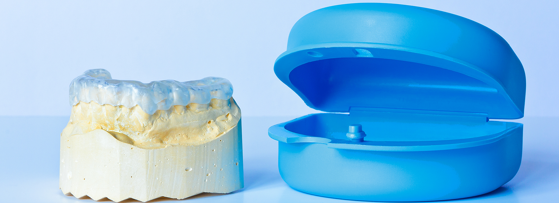 The image displays a dental implant on the left side and a blue plastic model of a human head with teeth on the right, placed against a white background.