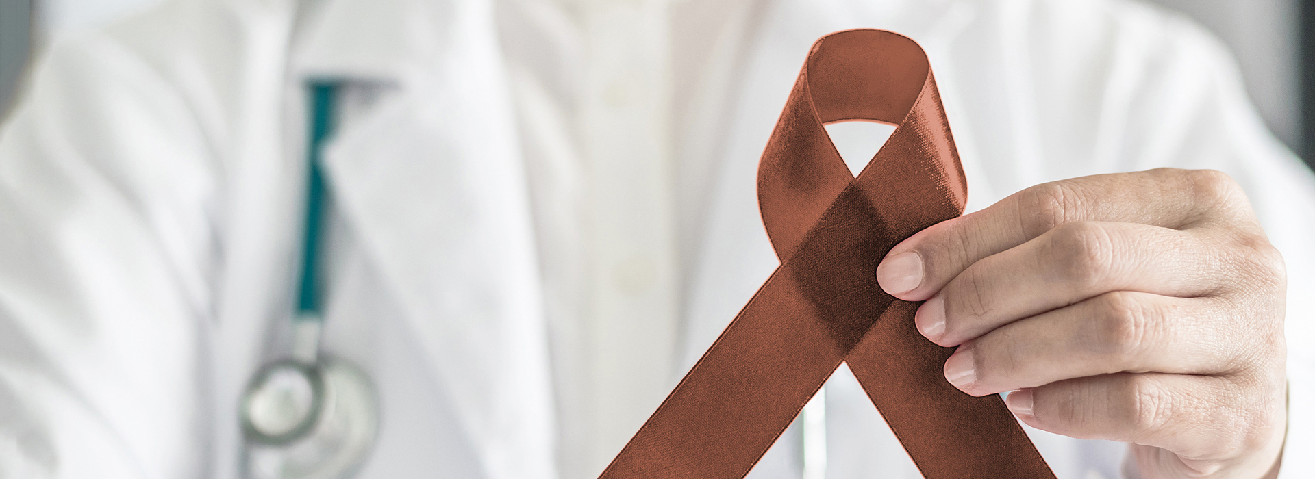 The image depicts a medical professional holding up an orange ribbon with a brown bow on top, symbolizing awareness for cancer.