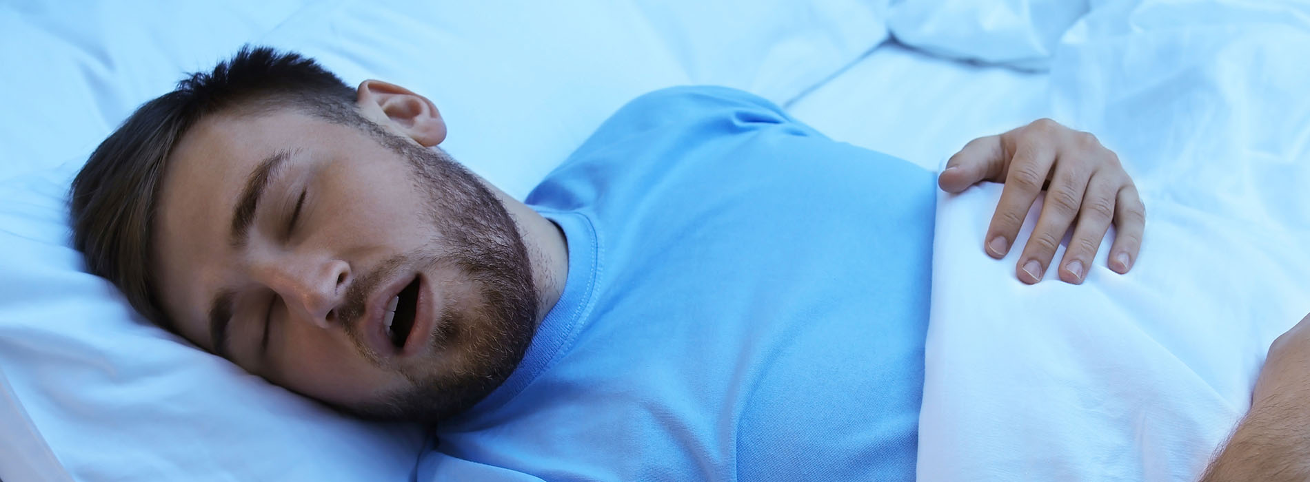 The image shows a man lying in bed with his eyes closed, appearing to be asleep or resting.