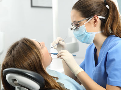 Dental hygienist performing procedure on patient s teeth while seated in dental chair.