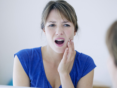 Woman with mouth open, showing teeth, looking at her reflection in mirror.