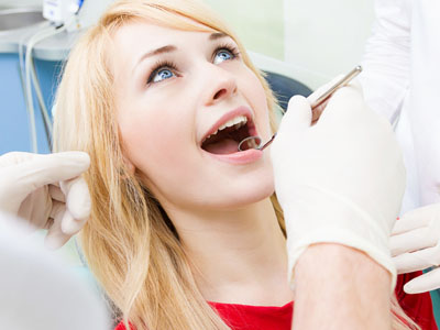 The image shows a woman with open mouth undergoing dental care, with a dentist performing a procedure while wearing gloves and a surgical mask.