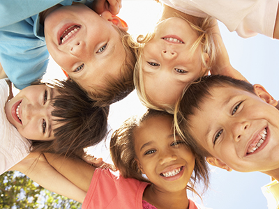 The image depicts a group of children happily posing together with their arms around each other, under a clear sky.