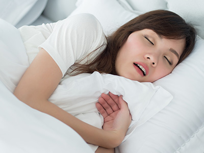 A woman sleeping peacefully in bed with her eyes closed and mouth slightly open.