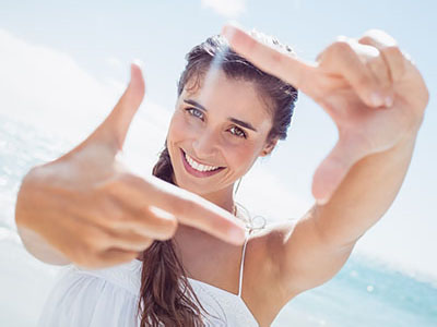 A woman with long hair is smiling at the camera while holding up her index finger.